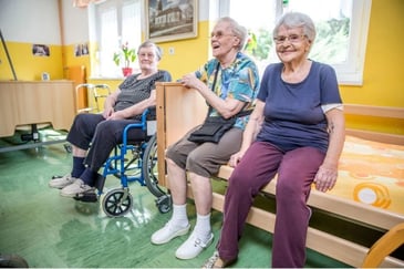 Three elderly care home residents sitting on a bed that has safe bed rails from being serviced by Hcsuk.