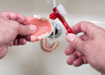 Someone cleaning their denture with a toothbrush showing best practices of denture care. 