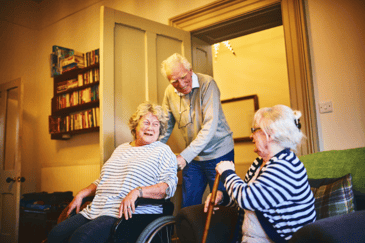 Three elderly people sat down in a care home with smiles on their face after the challenges with the care equipment was fixed.